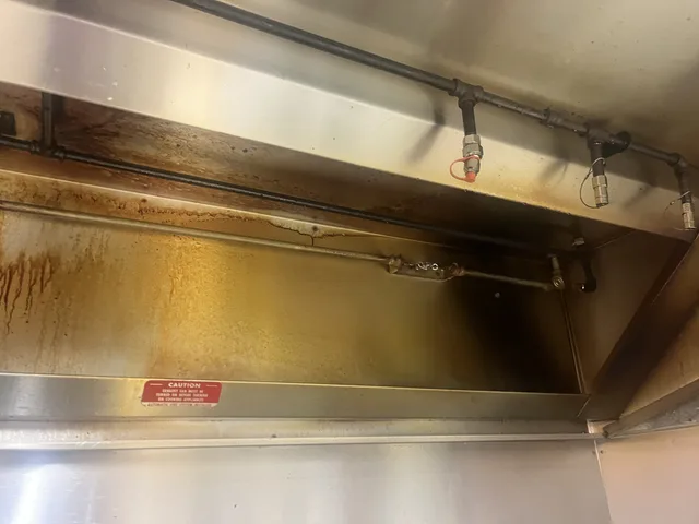 Grease buildup on the right interior wall of the hood, beneath the suppression pipework.